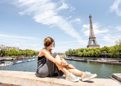 Junge stilvolle Frau mit herrlichem Blick auf den Eiffelturm auf der Brücke in Paris | © Gettyimages.com/RossHelen