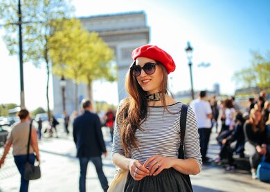 Vintage-getoentes Bild einer jungen Touristin, die an einem hellen und sonnigen Tag in Paris, Frankreich, im Stadtzentrum in der Naehe des Arc de Triomphe spazieren geht und sich entspannt. Sie traegt ein modisches, aber laessiges Streetstyle-Outfit, ein gestreiftes Hemd und einen Rock und geht die Strasse Champs-Élysées entlang. Moderner Lifestyle, lässige Mode, Entspannung in den Sommerkonzepten. | © Gettyimages.com/lechatnoir