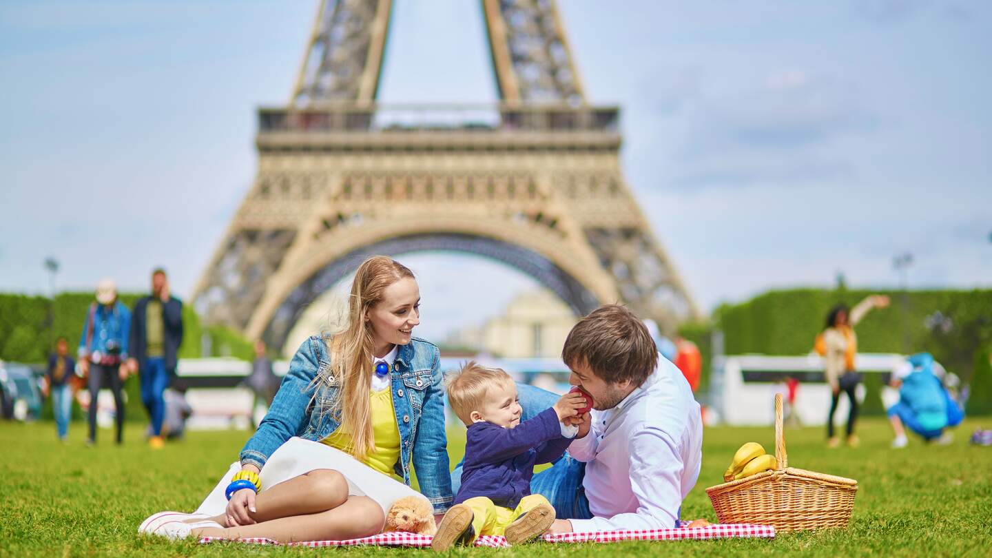 Glueckliche dreikoepfige Familie, Mutter, Vater und kleiner Kleinkindjunge, beim Picknick in Paris in der Nähe des Eiffelturms | © Gettyimages.com/encrier