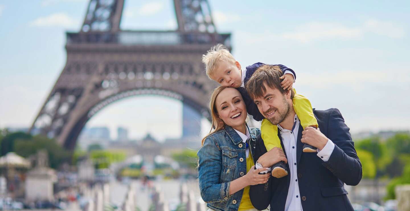 Glueckliche dreikoepfige Familie, die gemeinsam Spass in Paris in der Naehe des Eiffelturms hat | © Gettyimages.com/encrier