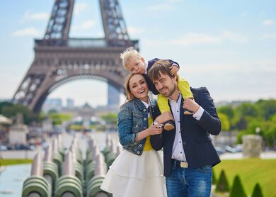 Glueckliche dreikoepfige Familie, die gemeinsam Spass in Paris in der Naehe des Eiffelturms hat | © Gettyimages.com/encrier