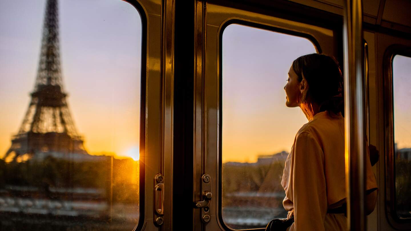 Eine Frau schaut aus der U-Bahn auf den Eiffelturm, während der Sonnenaufgang die Pariser Skyline erleuchtet, eine ruhige und malerische Morgenstimmung in der französischen Hauptstadt. | © Gettyimages.com/RossHelen