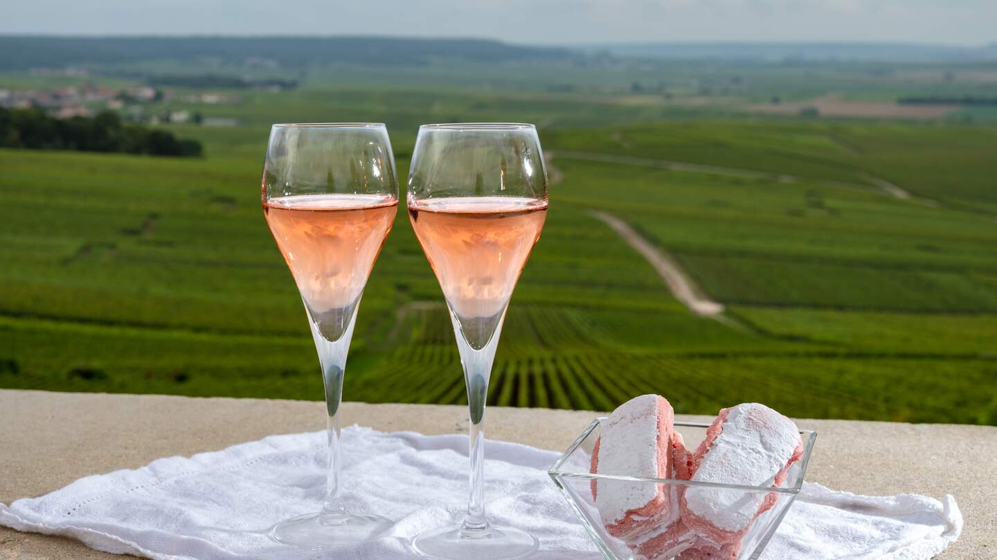  Rosen-Brut-Champagnerwein und Rosenkekse und Blick auf grüne Pinot Noir Grand Cru-Weinberge berühmter Champagnerhäuser in Montagne de Reims | © Gettyimages.com/barmalini