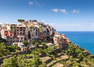 Corniglia, das malerische Dorf der Cinque Terre, thront auf hohen Felsen über dem Ligurischen Meer, während die Sonne die bunten Häuser zum Leuchten bringt. | © Gettyimages.vom/samvaltenbergs