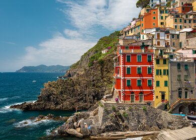 Blick vom Meer auf das Dorf Riomaggiore in der Cinque Terre, Italien, bei sonnigem Wetter, mit den charakteristischen bunten Häusern und dem Hafen. | © Gettyimages.com/StevanZZ
