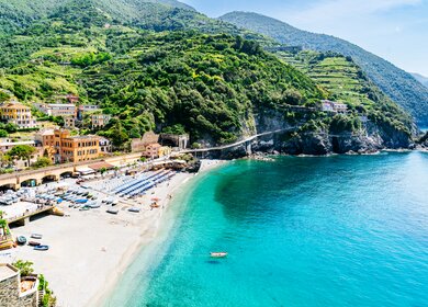 Blick auf das bunte Dorf und den Sandstrand in Monterosso, Cinque Terre, Italien, mit dem türkisblauen Meer und den grünen Weinbergen im Hintergrund. | © Gettyimages.com/Andrey Danilovich