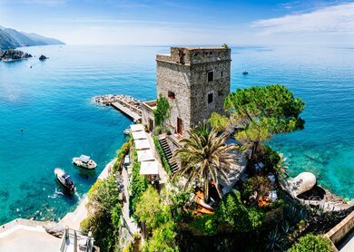 Mittelalterlicher Turm, der auf einem felsigen Vorsprung in Monterosso al Mare, Cinque Terre, Italien, thront und einen atemberaubendem Blick auf das azurblaue Meer und die grünen Hügel der ligurischen Küste im Hintergrund bietet | © Gettyimages.com/Andrey Danilovich