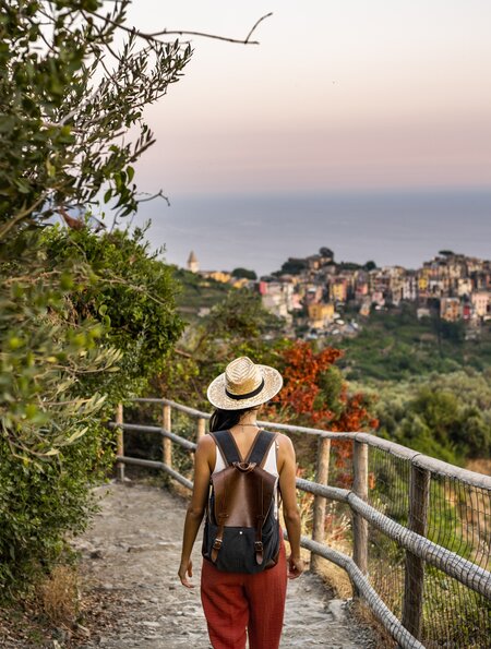 Eine Frau wandert auf einem schmalen Pfad mit atemberaubendem Blick auf das Küstendorf Corniglia in der Cinque Terre während die Sonne untergeht. | © Gettyimages.com/MStudioImages