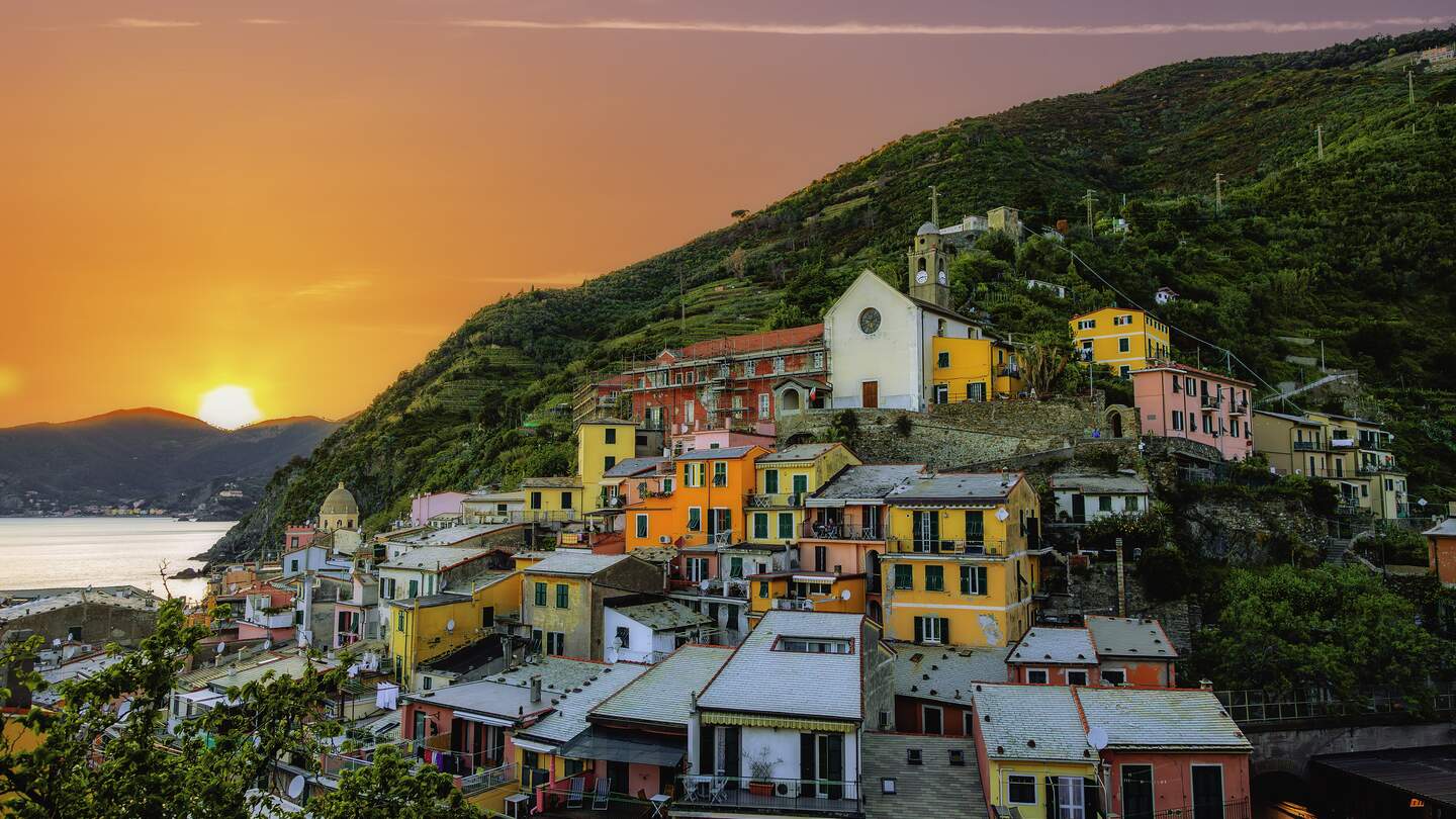 Farbenfrohe Luftaufnahme des Dorfes Vernazza in der Cinque Terre, Italien, mit Blick auf die bunten Häuser, das Ligurische Meer und die umliegenden Berge im warmen Licht des Sonnenuntergangs. | © Gettyimages.com/serts