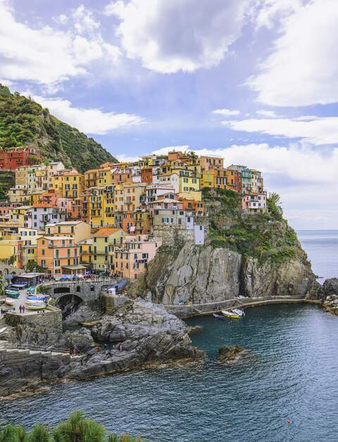 Panorama von Manarola, dem Cinque Terre Dorf in Ligurien, Italien, mit einem bewölkten Himmel, den bunten Häusern des Dorfes und den umliegenden Weinbergen. | © Gettyimages.com/serts