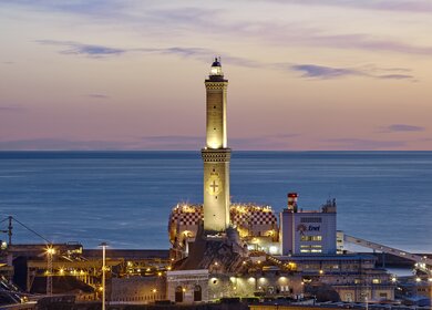 Blick auf das Meer und die Stadt mit dem Leuchtturm von Genua (Lanterna di Genova) bei Sonnenaufgang. Wahrzeichen und Sehenswürdigkeit in der Hafenstadt. | © Gettyimmages.com/luiginophoto
