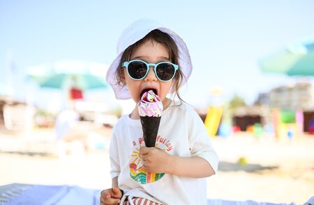 Lächelndes Kind mit einem leckeren Eis am sonnigen Strand in Italien, Meer im Hintergrund | © Gettyimages.com/Yuliya Taba