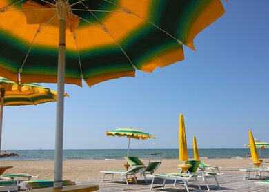 Liegestühle unter einem Sonnenschirm am Sandstrand von Rimini, Italien, mit Blick auf das Meer | © Gettyimages.com/ChiccoDodiFC