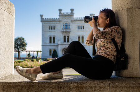 Eine Touristin fotografiert das Schloss Miramare (Castello di Miramare) in Triest, eine beeindruckende Sehenswürdigkeit, die sich auf einer Klippe über dem Meer befindet. | © Gettyimages.com/Dusan Stankovic