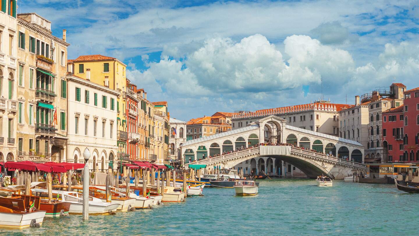 Im Hintergrund die Rialtobruecke mit Touristen, im Vordergrund anliegende Boote auf dem Canal Grande in Venedig. | © Gettyimages.com/mammuth
