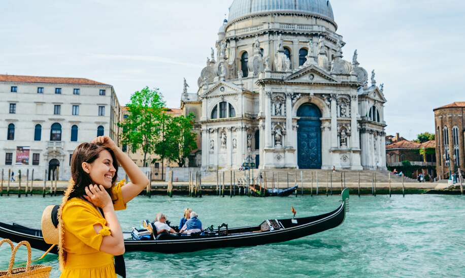 Frau im gelben Sonnenkleid sitzt am Ufer mit Blick auf den grossen Kanal in Venedig. | © Gettyimages.com/Vera_Petrunina