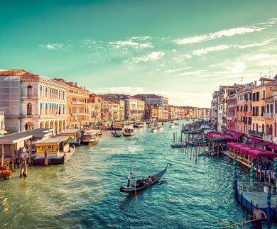 Ein Gondelfahrer paddelt in Richtung des Sonnenuntergangs auf dem grossen Kanal von Venedig. Aufnahme von der Rialto-Bruecke | © Gettyimages.com/JaCZhou