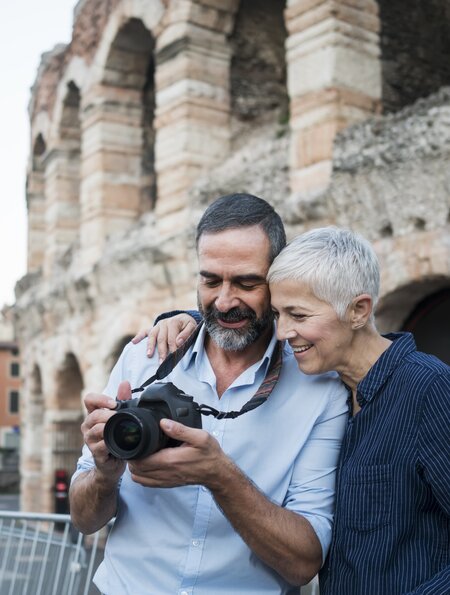 Mann und Frau in Verona, der Mann trägt eine Kamera um den Hals und sie schaut mit ihm darauf | © Gettyimages.com/Vesnaandjic