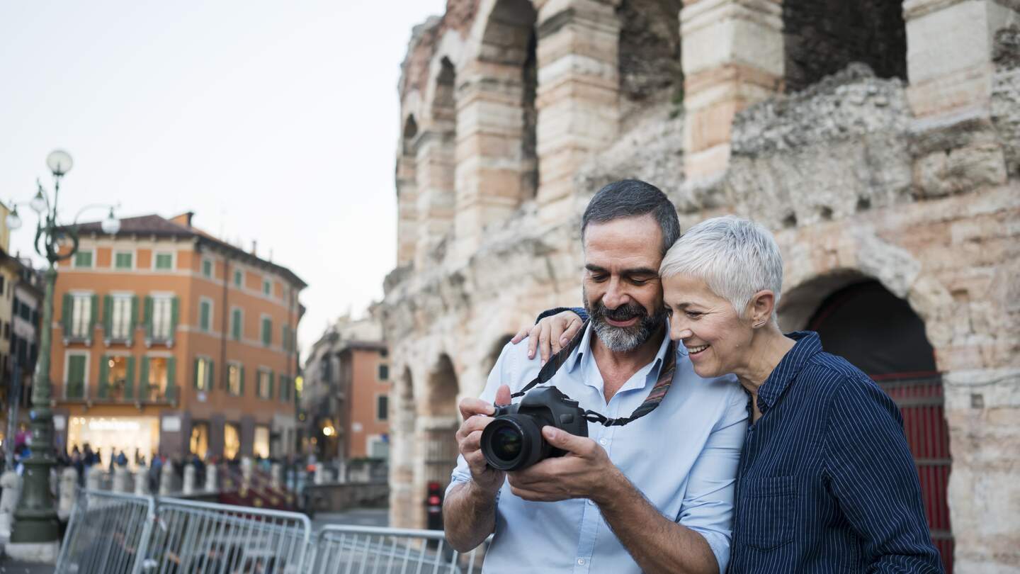 Mann und Frau in Verona, der Mann trägt eine Kamera um den Hals und sie schaut mit ihm darauf | © Gettyimages.com/Vesnaandjic