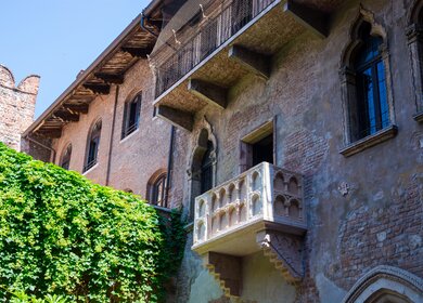 Untersicht auf den Balkon in Julias Haus und Innenhof in Verona im Sommer mit hellblauem Himmel | © GettyImages.com/alla_iatsun
