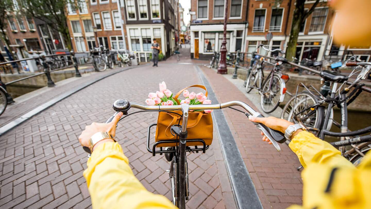 eine Person, die mit einem Fahrrad durch eine Strasse in Amsterdam faehrt | ©  Gettyimages.com/RossHelen