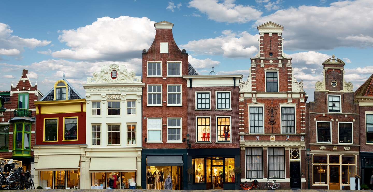 Stadtszene Amsterdam mit liebevoll restaurierten Giebelhäusern und kleinen Ladengeschaeften an einer Grachtenbruecke | © Gettyimages.com/MediaProduction
