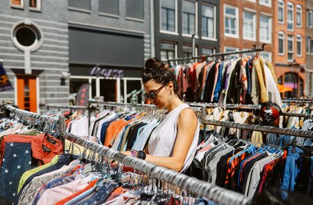 Frau mit Sonnenbrille und ärmelloser Bluse schaut durch die Kleiderstaender eines Flohmarktes in Amsterdam | © Gettyimages.com/lechatnoir