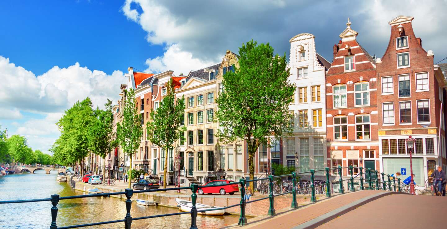 Blick auf die Amstel und eine Bruecke mit einer historischen Strassenlaterne im linken Vordergrund | © Gettyimages.com/adisa