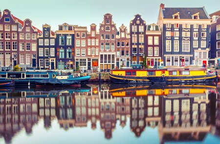 Amsterdams traditionelle Haeuserarchitektur mit Hausbooten spiegelt sich am fruehen Morgen in einer Gracht | © Gettyimages.com/KavalenkavaVolha