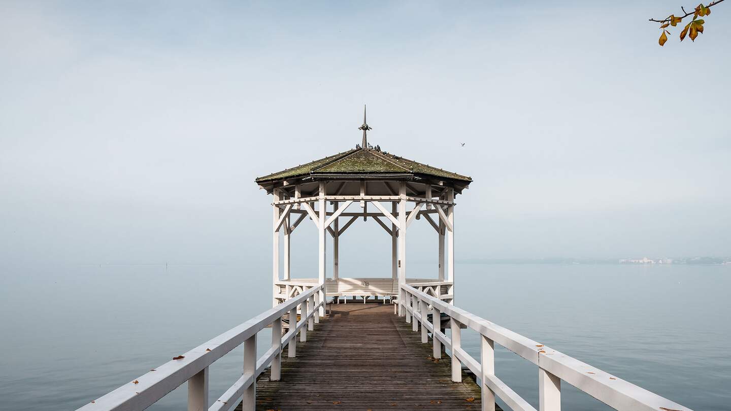 Holzsteg, der zu einem Pavillon mit Spitzdach fuehrt, der auf einem Wasserbecken steht.  | © gettyimages.com/Andrii Baidak