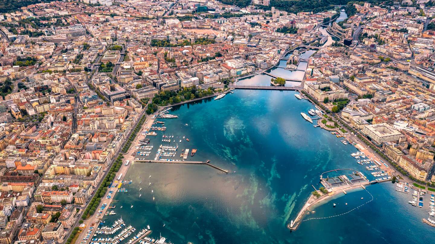 Blick aus einem hohen Winkel auf das Panorama der Stadt Genf vom Drohnenpunkt am Morgen mit der Spiegelung des Himmels am Genfersee | © Gettyimages.com/JaCZhou
