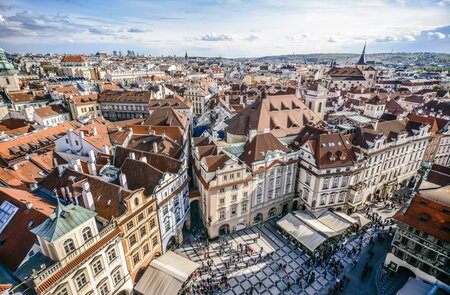 Luftaufnahme über die orangefarbenen Daecher des Altstaedter Rings in Prag, Touristen stehen auf dem Platz im Vordergrund. | © Gettyimages.com/AleksandarGeorgiev