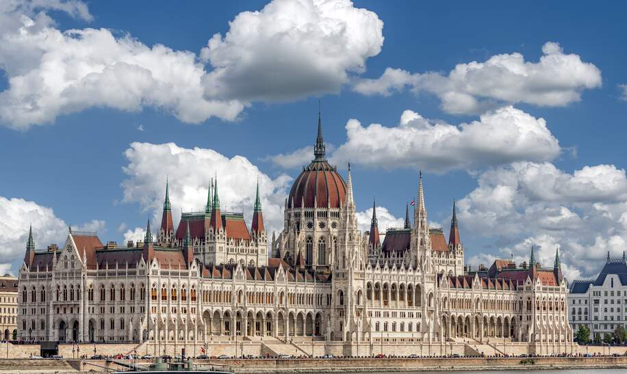 Schraegansicht der Aussenfassade des ungarischen Parlamentsgebaeudes in Budapest an der Donau mit blauem Himmel und Schoenwetterwolken | © GettyImages.com/Frank Wagner