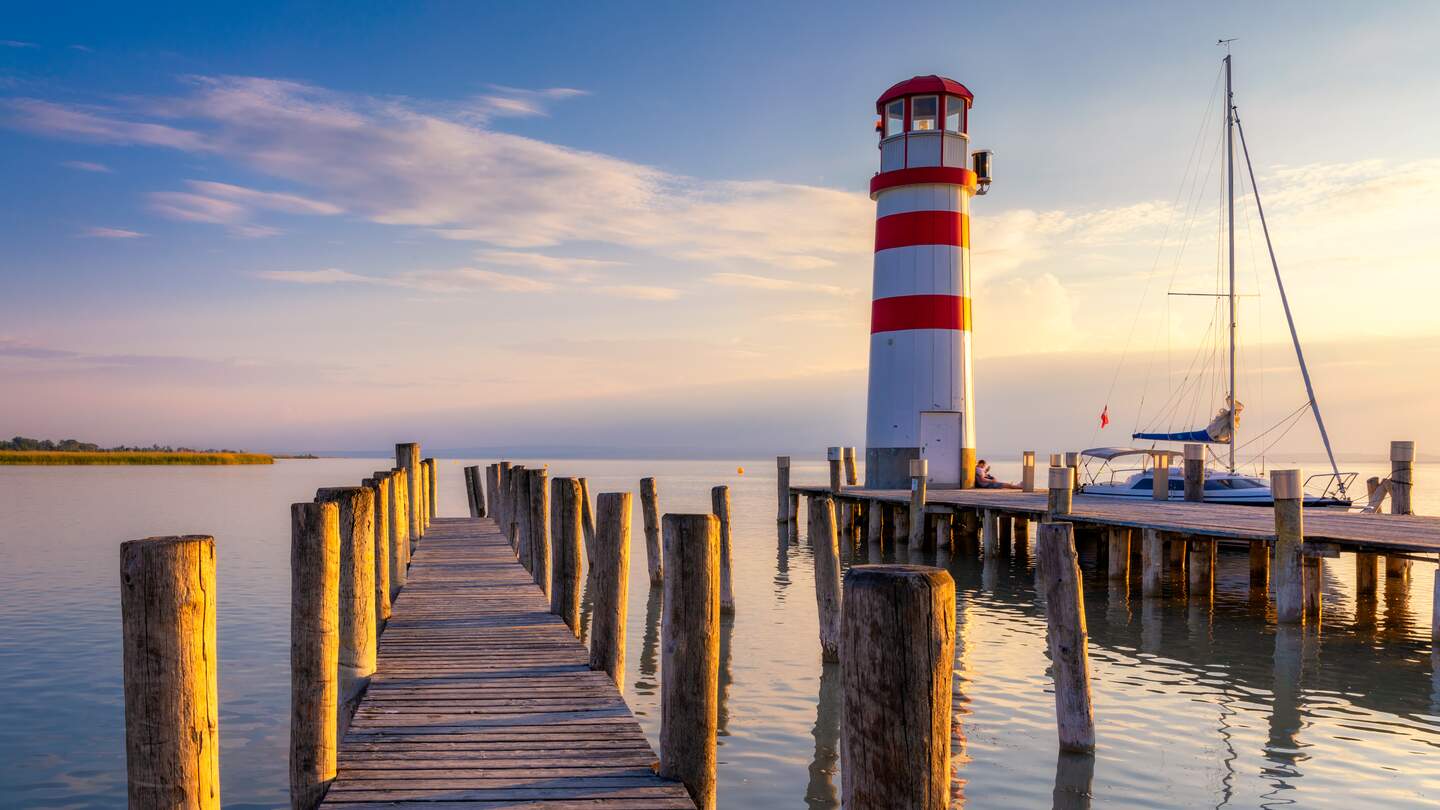 Holzsteg mit Leuchtturm in Podersdorf am Neusiedler See in Oesterreich bei Sonnenuntergnag | © Gettyimages.com/DaLiu