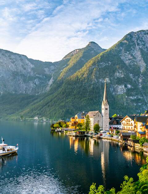 Panoramablick auf die beruehmte Alte Hallstatt und den alpenlaendischen tiefblauen See mit Touristenschiff im malerischen goldenen Morgenlicht | © Gettyimages.com/eugen-b