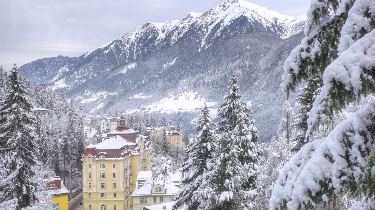 Verschneites Panorama von Bad Gastein im Winter, mit Gebäuden, die sich an den Berghang schmiegen, umgeben von schneebedeckten Alpen | © Gettyimages.com/DaveLongMedia