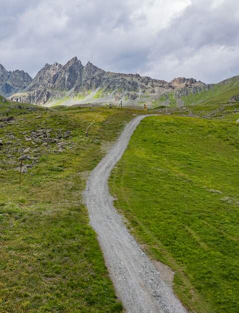 Schoene Rad- und Wanderroute in der Silvretta Arena in Ischgl. Mit der majestaetischen Bergkette im Hintergrund und auch ein Stueck einer Bergstation im schoenen Wolkenhimmel. Es gibt auch ein paar gelbe Schneekanonen im Hintergrund. | © Gettyimages.com/amessink