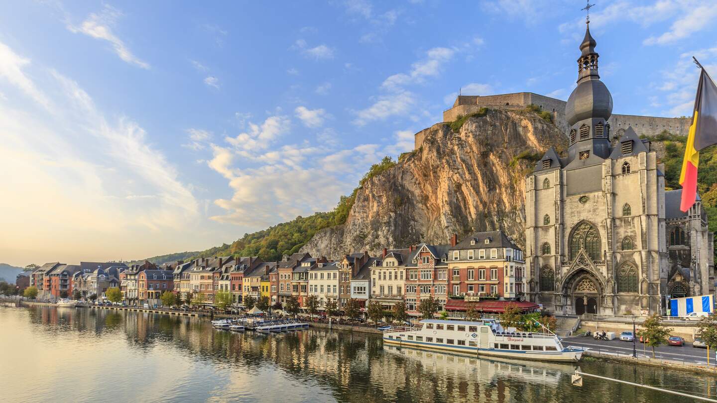 Dinant, bunte Häuser entlang eines Flusses mit einer Kirche und einer Festung auf einem Hügel im Hintergrund | © GettyImages.com/Flavio Vallenari