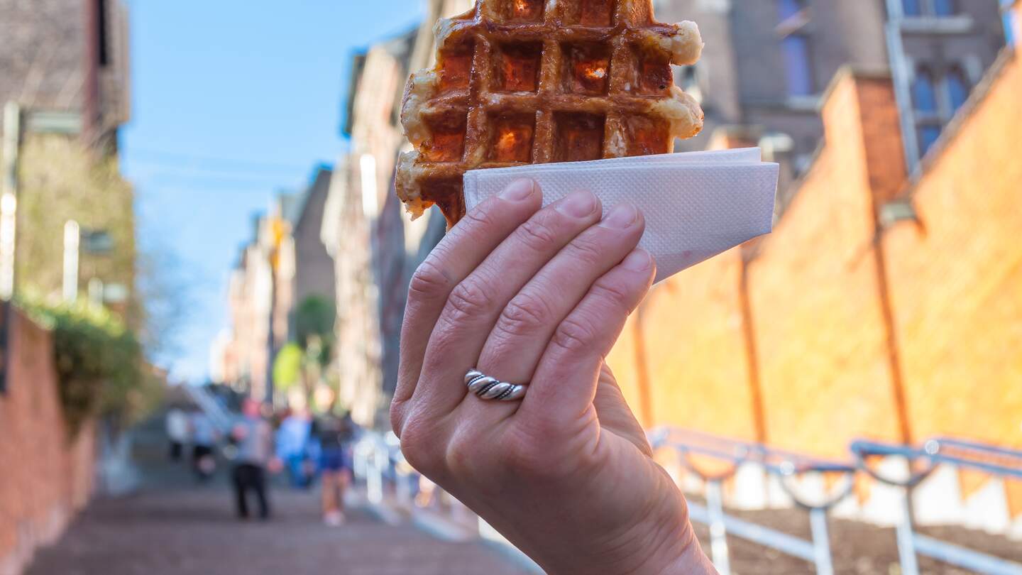 Belgische Waffel vor dem verschwommenen Hintergund der Montagne de Bueren Treppe in Lüttich | © Gettyimages.com/MilosRuzicka