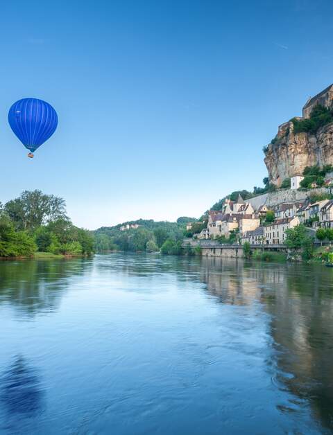 Chateaux Beynac auf einer Klippe, auf der linken Seite fliegt ein blauer Heissluftballon | © Gettyimages.com/garethkirklandphotogrphy
