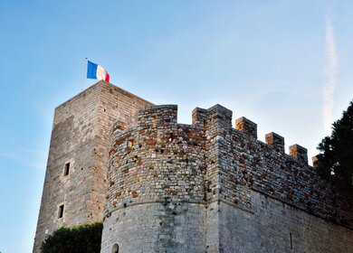 Untersicht auf das von der Sonne angestrahlte Musée de la Castre mit Frankreichflagge in Cannes | © Gettyimages.com/maudanros