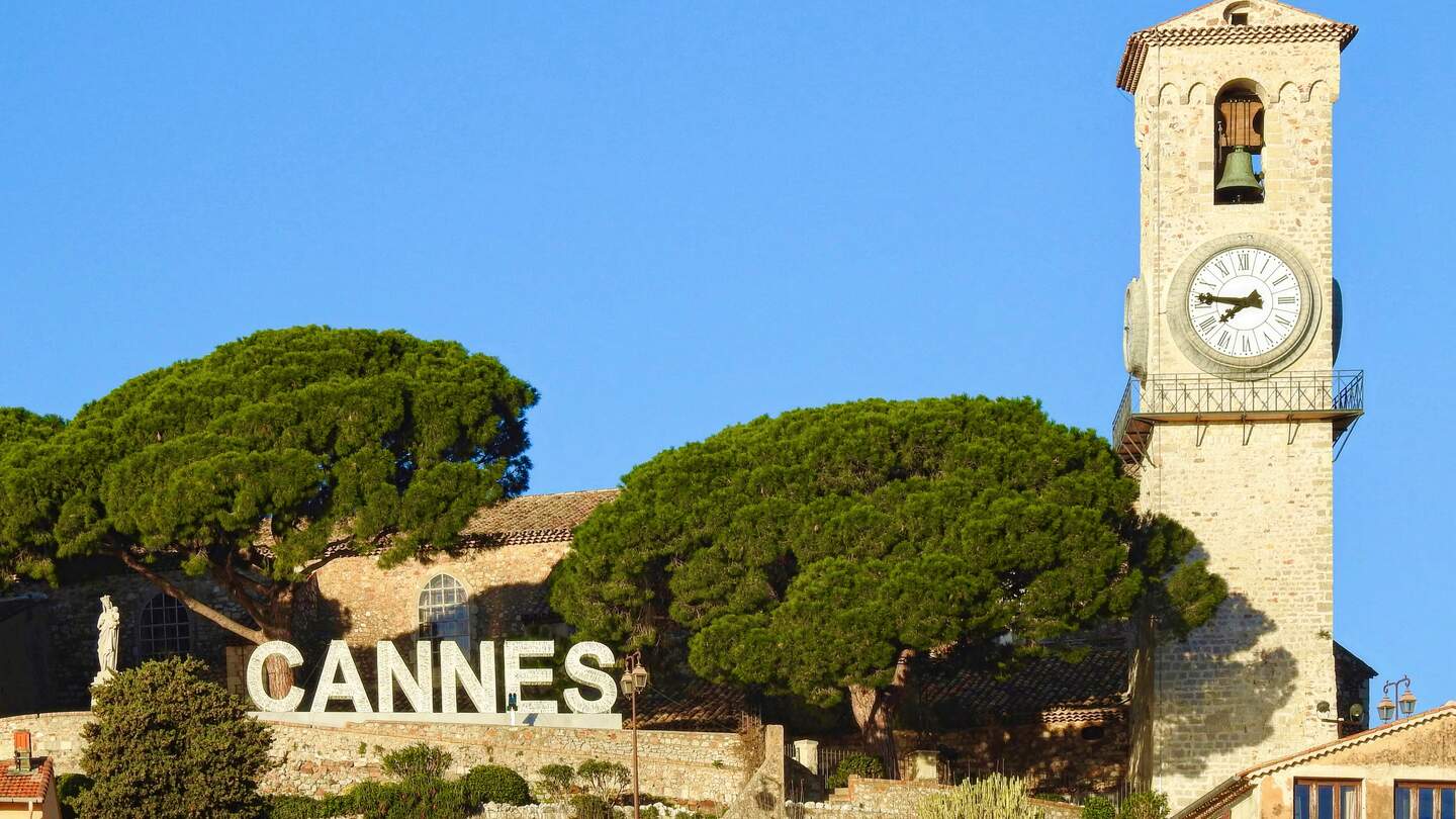 Église Notre-Dame d’Esperance, oben auf Le Suquet Cannes, mit dem Cannes-Schild an einem klaren, sonnigen Tag mit blauem Himmel | © Gettyimages.com/AngelaHarrodPhotography