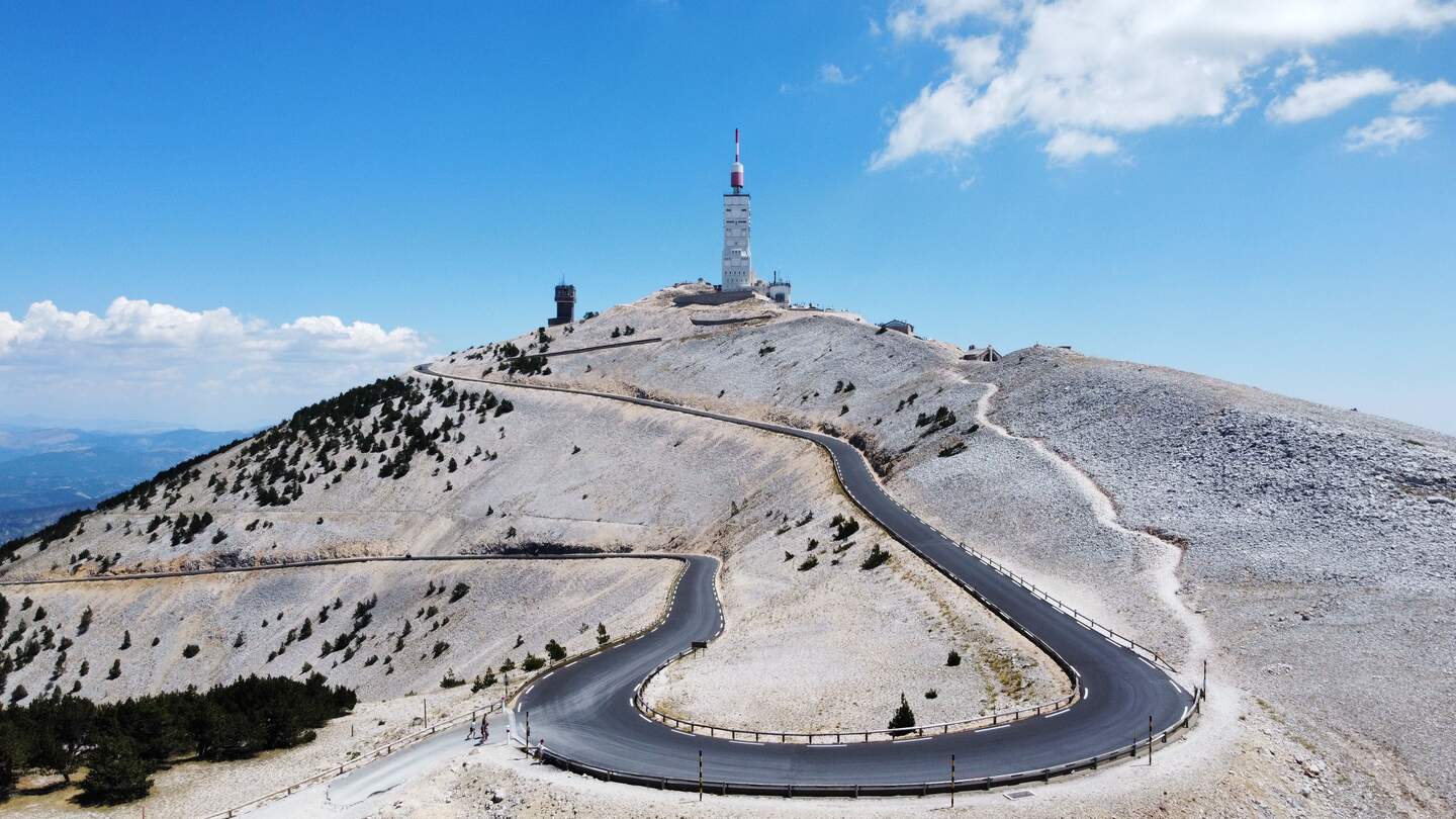 Eine schmale Autobahn, die zum Mont Ventoux in Frankreich fuehrt, mit blauem Himmel im Hintergrund | © Gettyimages.com/wirestock