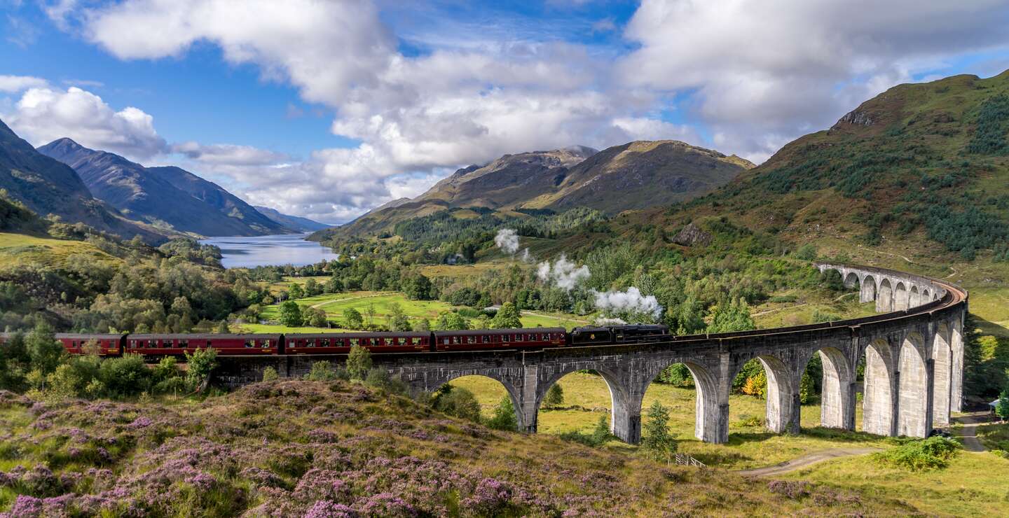 Beruehmten Glenfinnan Eisenbahnviadukt in Schottland. Ein Zug faehrt gerade ueber das gigantische Bauwerk mit atemberaubenden Hintergrund | © Gettyimages:com/catuncia