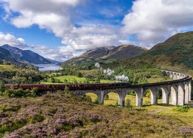 Beruehmten Glenfinnan Eisenbahnviadukt in Schottland. Ein Zug faehrt gerade ueber das gigantische Bauwerk mit atemberaubenden Hintergrund | © Gettyimages:com/catuncia