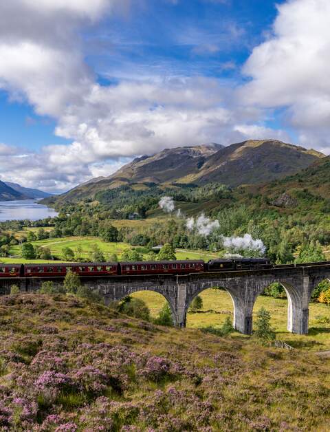 Beruehmten Glenfinnan Eisenbahnviadukt in Schottland. Ein Zug faehrt gerade ueber das gigantische Bauwerk mit atemberaubenden Hintergrund | © Gettyimages:com/catuncia