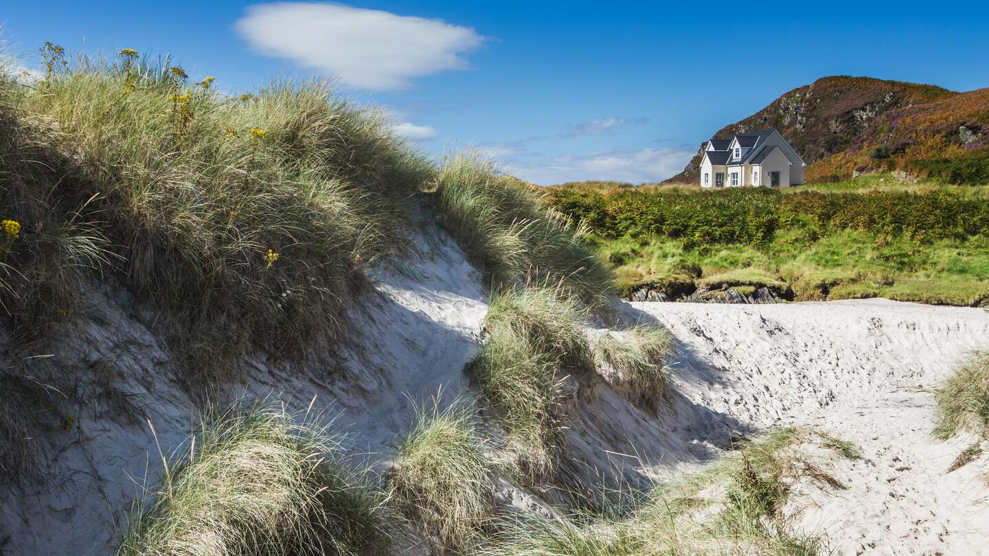 Weißer Sandstrand in Morar an der Westküste Schottlands mit einem Cottage auf der einer Düne im Hintergrund | © GettyImages.com/FedevPhoto