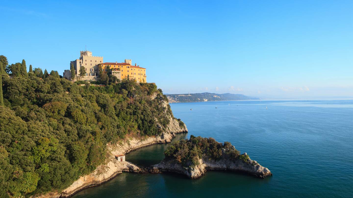 Blick auf das Schloss Duino vom Meer aus mit,der mit Baeumen bewachsenen, Kueste | © Gettyimages.com/Bepsimage
