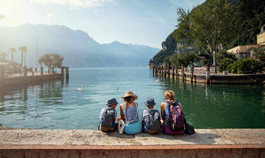 Familie sitzen im Hafen von Riva del Garda und geniessen die Aussicht auf den Gardasee, vor ihnen schwimmt ein Schwan. Im Hintrgrund entdeckt man die Bilder | © Gettyimages.com/imgorthand