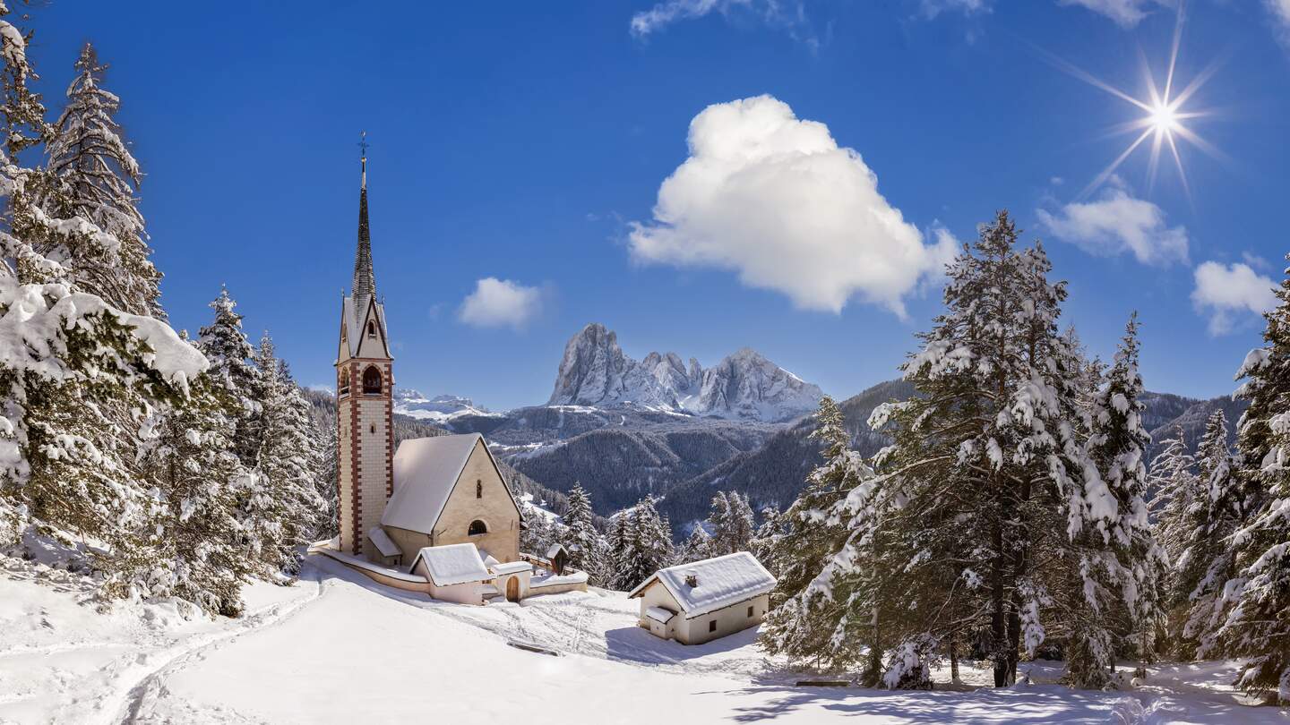 St. Jakobskriche in Groeden bei dem fruehgeschichtlichen Hoehenweg Troi Paian im Schnee bei Sonnenschien und leichten Wolken | © Gettyimages.com/DieterMeyrl